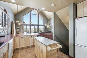 Kitchen with light tile patterned flooring, dishwashing machine, refrigerator, and ceiling fan with notable chandelier