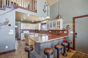 Kitchen with white appliances, a kitchen breakfast bar, backsplash, light tile patterned floors, and kitchen peninsula