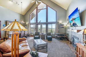 Carpeted living room featuring a tiled fireplace, high vaulted ceiling, ceiling fan with notable chandelier, and rail lighting