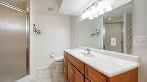 Bathroom with an enclosed shower, vanity, toilet, and tile patterned flooring