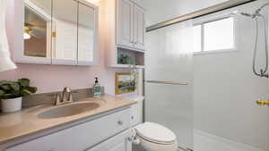 Bathroom with ceiling fan, tiled shower, vanity, and toilet