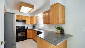 Kitchen with black appliances, granite counters, light tile patterned floors, and backsplash