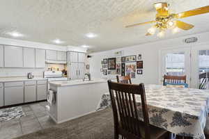 Kitchen featuring a textured ceiling, crown molding, light tile patterned flooring, ceiling fan, and sink