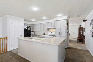 Kitchen featuring crown molding, dark carpet, a center island with sink, white appliances, and sink