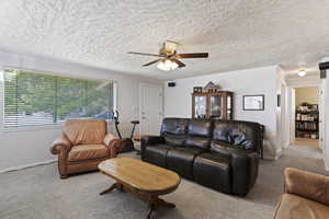 Living room featuring a textured ceiling, ornamental molding, ceiling fan, and carpet floors