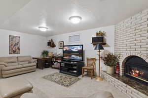 Carpeted living room featuring brick wall, a textured ceiling, and a brick fireplace