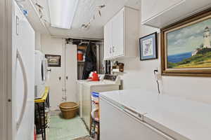 Clothes washing area with cabinets, a textured ceiling, and washing machine and dryer