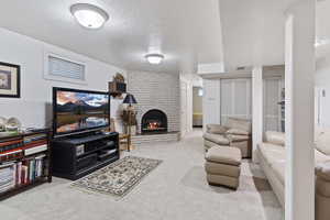 Living room with a fireplace, a textured ceiling, light colored carpet, and brick wall