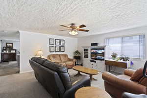 Carpeted living room with ceiling fan and a textured ceiling