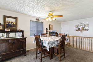 Dining space with ceiling fan, a textured ceiling, ornamental molding, and light carpet