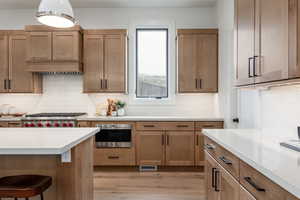 Kitchen with decorative backsplash, light hardwood / wood-style floors, a kitchen bar, and stainless steel oven