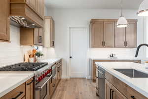 Kitchen with premium range hood, hanging light fixtures, sink, appliances with stainless steel finishes, and light hardwood / wood-style floors