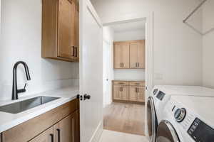 Laundry area with light wood-type flooring, washer and clothes dryer, sink, and cabinets