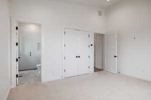 Unfurnished bedroom with light carpet, a towering ceiling, ensuite bath, and a closet