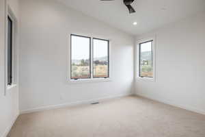 Empty room featuring vaulted ceiling, ceiling fan, and light colored carpet