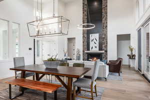 Dining room featuring a notable chandelier, light hardwood / wood-style floors, a fireplace, and a high ceiling