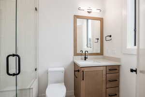 Bathroom featuring vanity, a shower with shower door, and toilet