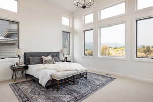 Carpeted bedroom featuring a notable chandelier, a towering ceiling, and multiple windows