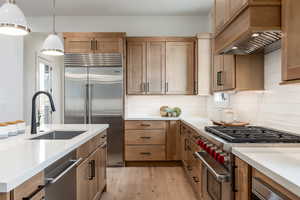 Kitchen with light wood-type flooring, a wealth of natural light, hanging light fixtures, high quality appliances, and premium range hood