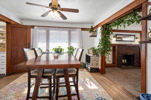 Dining space with ceiling fan, hardwood floor, and a brick fireplace