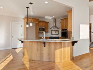 Kitchen with hardwood  flooring, appliances with stainless steel finishes, pendant lighting, exhaust hood, and backsplash