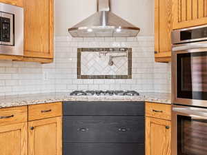 Kitchen with decorative backsplash, appliances with stainless steel finishes, ventilation hood, granite counters, gas range, pot-filler