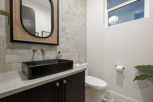 Powder Bathroom with toilet, backsplash, tile patterned flooring, tile walls, and vanity