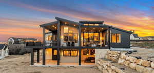 Back house at dusk featuring a patio and a balcony