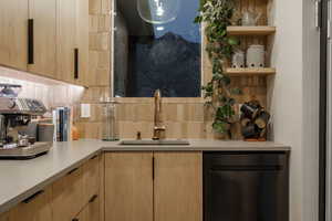 Butlers pantry with light brown cabinetry, decorative backsplash, stainless steel dishwasher, and sink