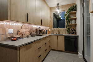 Butlers pantry featuring hanging light fixtures, dishwasher, sink, light tile patterned floors, and decorative backsplash