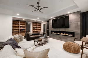 Living room with built in features, a tile fireplace, and a raised ceiling