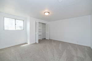 Unfurnished bedroom with a textured ceiling, light carpet, and a closet