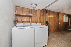 Laundry area with a textured ceiling, wooden walls, and light hardwood / wood-style floors