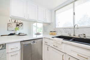 Kitchen featuring dishwasher, light stone counters, white cabinets, decorative backsplash, and kitchen peninsula