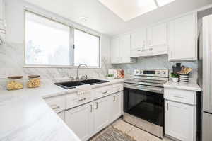 Kitchen with decorative backsplash, white cabinetry, stainless steel electric range, light tile patterned floors, and sink