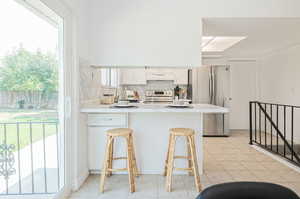 Kitchen with tasteful backsplash, a breakfast bar, light tile patterned flooring, appliances with stainless steel finishes, and white cabinets