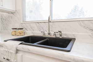 Interior details with tasteful backsplash, light stone countertops, sink, and white cabinetry