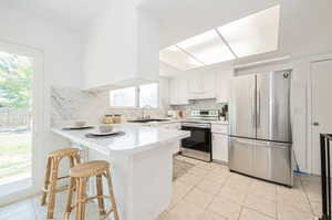 Kitchen with stainless steel appliances, white cabinets, light tile patterned floors, tasteful backsplash, and sink