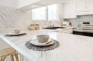 Kitchen featuring ventilation hood, sink, tasteful backsplash, white cabinetry, and range