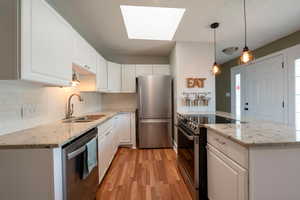 Kitchen featuring light wood-type flooring, sink, white cabinets, hanging light fixtures, and stainless steel appliances