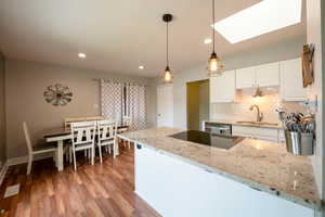 Kitchen featuring light hardwood / wood-style floors, white cabinetry, light stone counters, a skylight, and decorative light fixtures