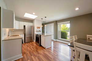 Kitchen with appliances with stainless steel finishes, hanging light fixtures, white cabinets, a skylight, and sink