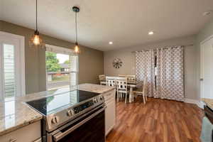 Kitchen with white cabinets, hanging light fixtures, hardwood / wood-style flooring, stainless steel appliances, and light stone countertops