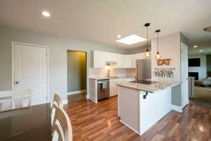 Kitchen with hardwood / wood-style flooring, appliances with stainless steel finishes, a breakfast bar, and white cabinetry