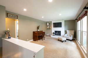 Living room featuring light carpet, a brick fireplace, a textured ceiling, and a healthy amount of sunlight