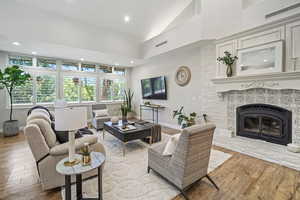 Living room featuring high vaulted ceiling, a stone fireplace, and wood-type flooring