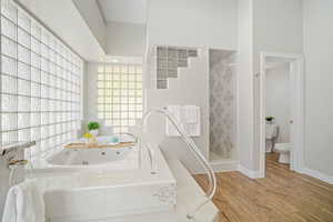 Bathroom featuring a relaxing tiled tub, toilet, and hardwood / wood-style flooring