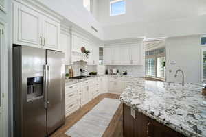 Kitchen with decorative backsplash, light stone counters, stainless steel appliances, and white cabinetry