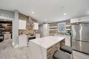 Kitchen with stainless steel fridge, backsplash, range with gas stovetop, and wall chimney exhaust hood