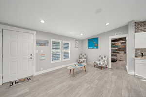 Sitting room featuring light wood-type flooring, vaulted ceiling, and brick wall